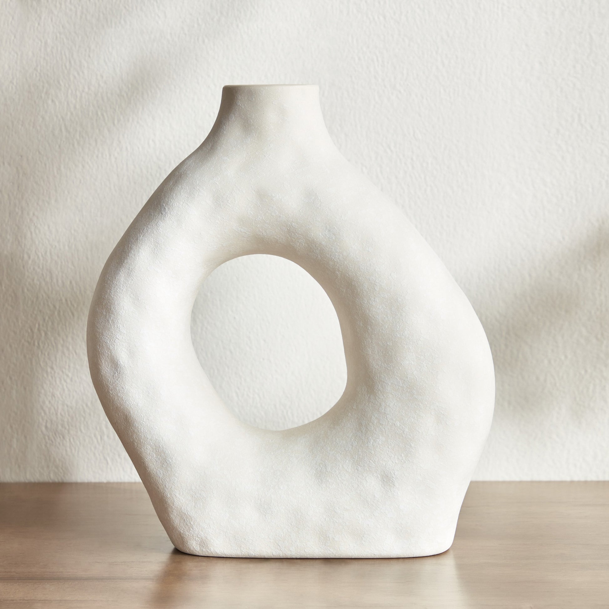 White ceramic vase with circular design on a neutral background