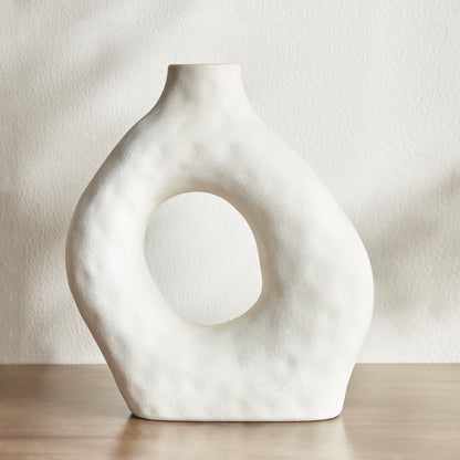 White ceramic vase with circular design on a neutral background