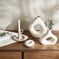 Set of white ceramic vases and candle holders on a wooden surface with a neutral background