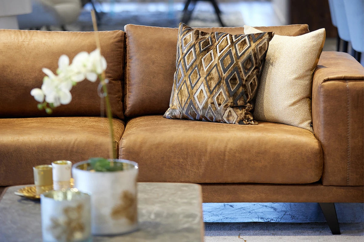 Brown sectional sofa with decorative pillows and a coffee table with candles and a plant.