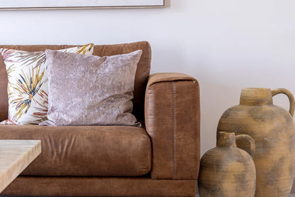 Brown leather sofa with decorative pillows and large ceramic vases against a white wall.