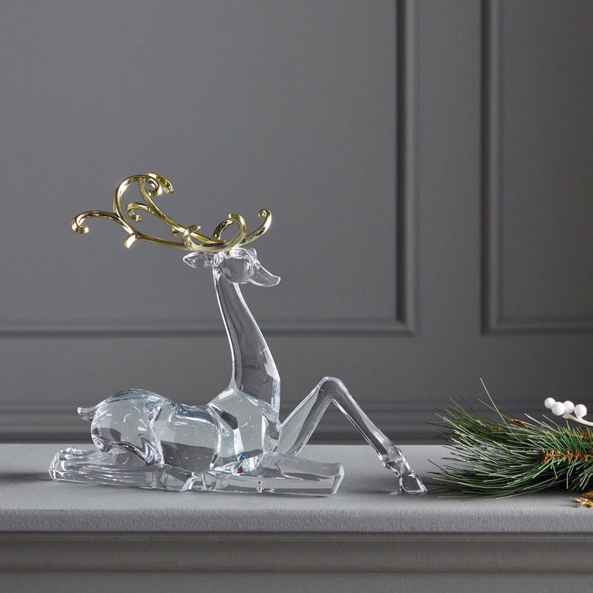 Clear glass deer figurine with gold antlers on a gray surface against a gray wall.