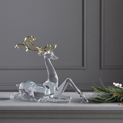 Clear glass deer figurine with gold antlers on a gray surface against a gray wall.
