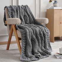 Gray knitted blanket draped over a beige armchair in a room with wooden furniture.
