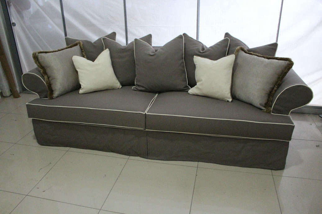 Gray sectional sofa with decorative pillows on a tiled floor. Roma Collection Sofa – Serene Comfort in a Chaotic World | Vella Concept