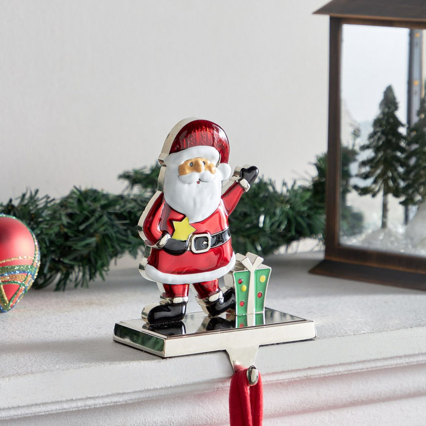 Decorative Santa Claus figurine with a gift on a white surface with Christmas decorations in the background.