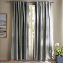 Gray curtains hanging in front of a window with a neutral wall and plant in the background