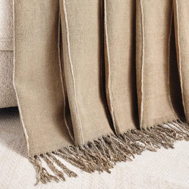 Beige woven blanket with fringes on a white surface
