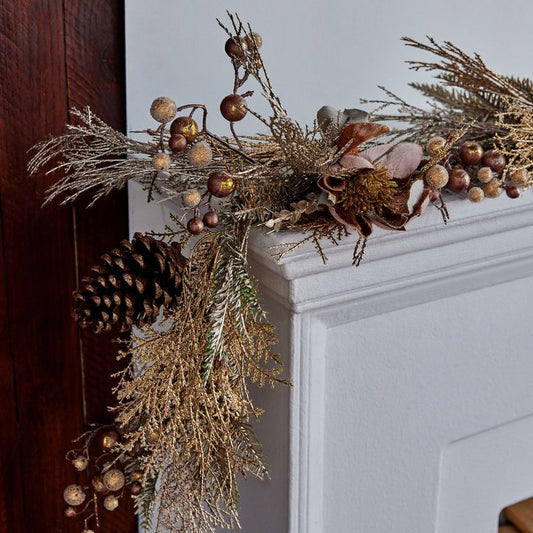 Decorative wreath with pinecones and branches on a fireplace mantle.