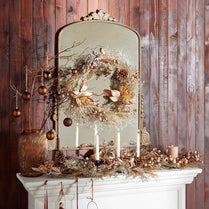 Decorative mantel with mirror, candles, and autumn-themed decorations against a wooden wall.