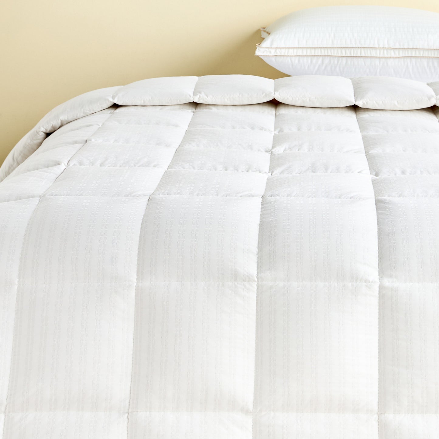 White comforter on a bed with pillows against a beige wall