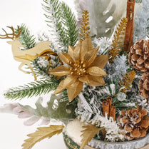Decorative arrangement with gold poinsettia, pine branches, cinnamon sticks, and pinecones on a white background.