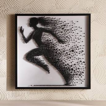 Framed artwork of a running person made from black dots on a white background, mounted on a textured beige wall.