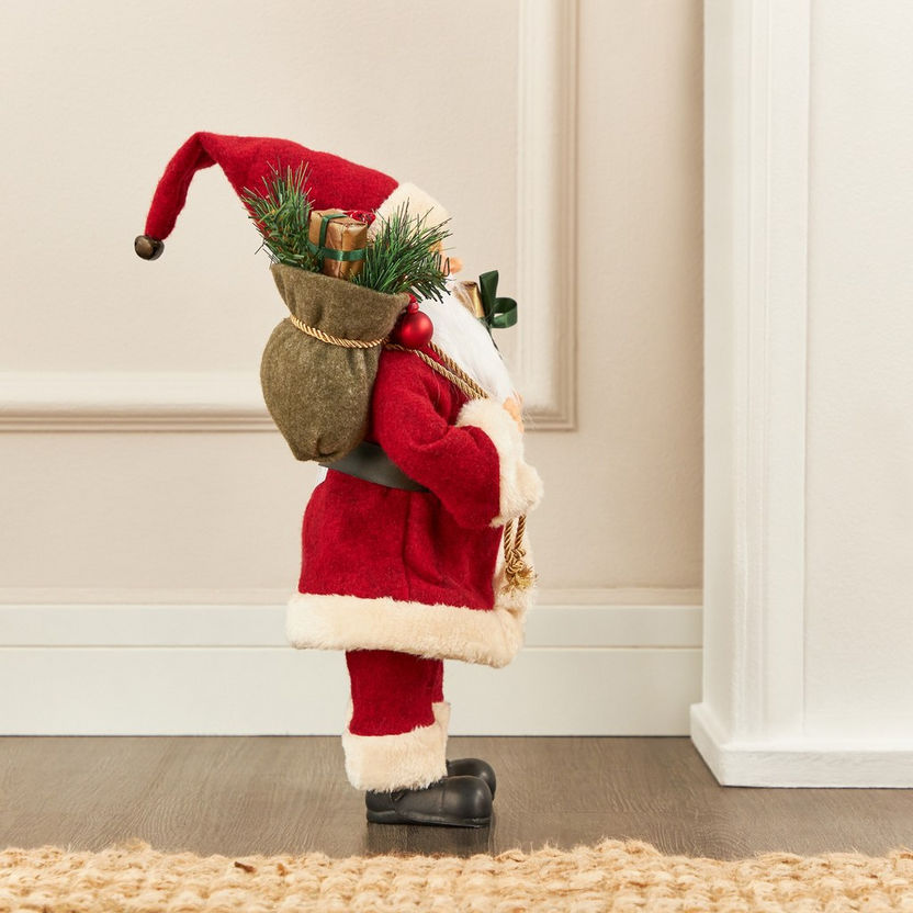 Decorative figure of a Santa Claus holding a sack with Christmas decorations against a neutral wall.