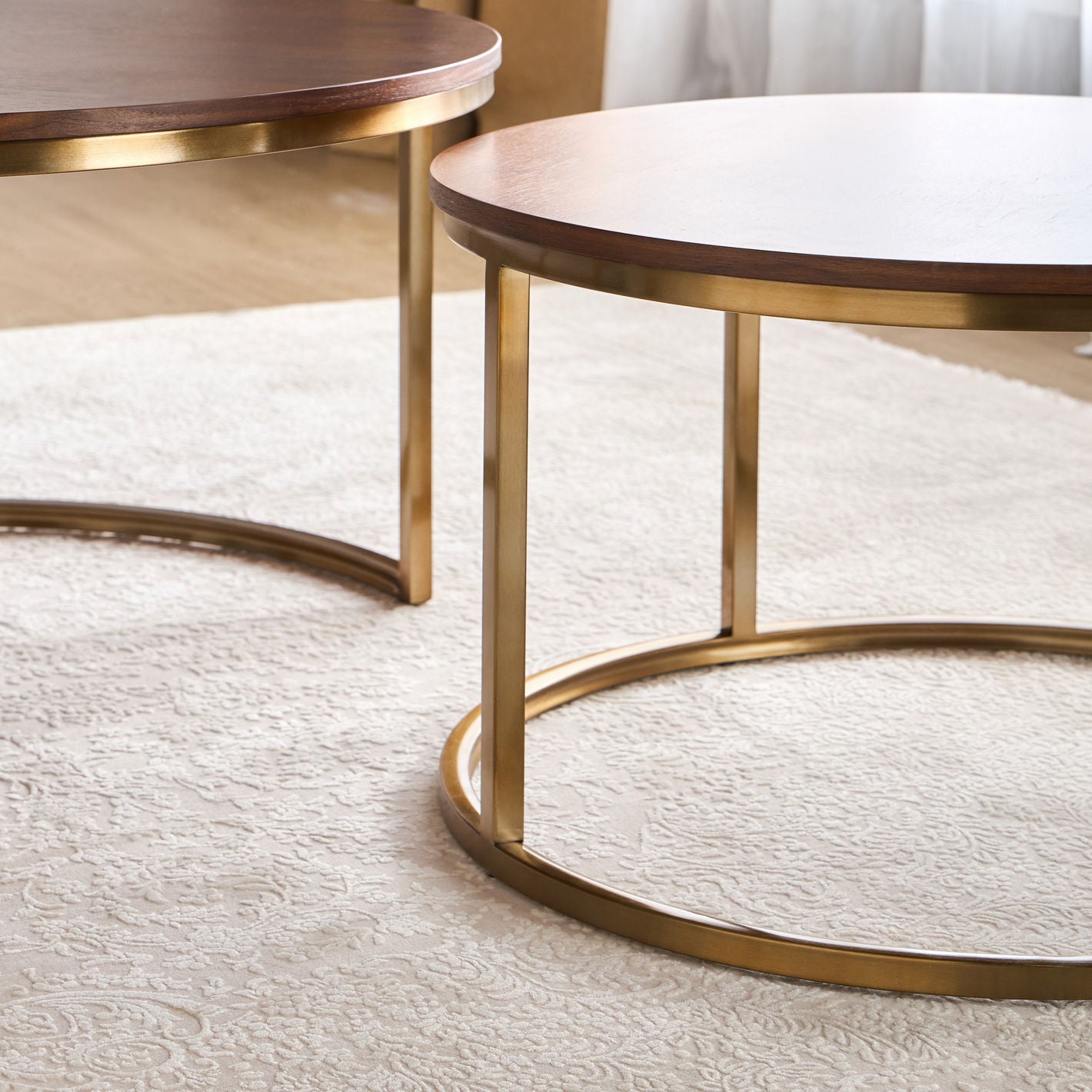 Two round wooden tables with gold metal bases on a light-colored rug.