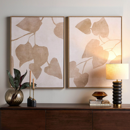 Two framed leaf-patterned artworks on a wall above a wooden console table with decorative items.