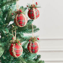 Red plaid Christmas ornaments with textured ribbons hanging on a tree.