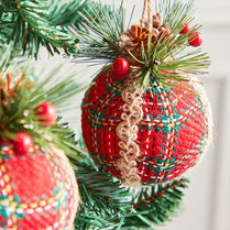 Red textured Christmas ornament with lace detail hanging on a tree branch.