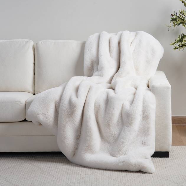 White fluffy blanket draped over a white sofa with a neutral background