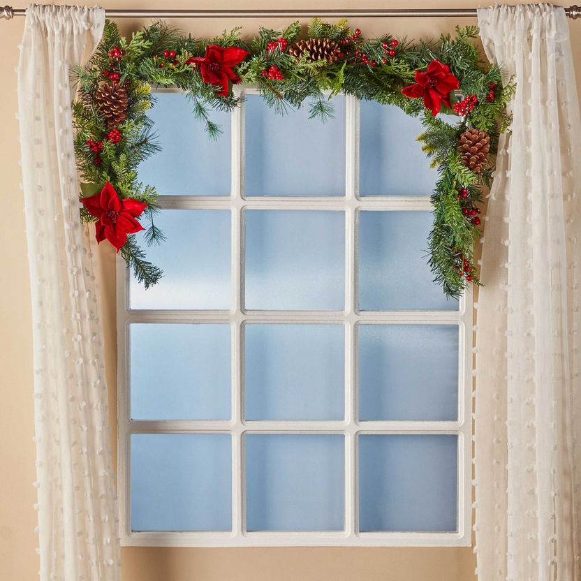 Decorative Christmas garland with red flowers and pine cones above a window.
