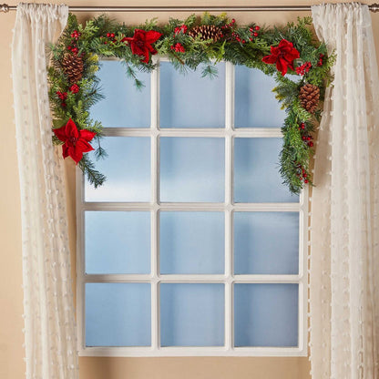 Decorative Christmas garland with red flowers and pine cones above a window.