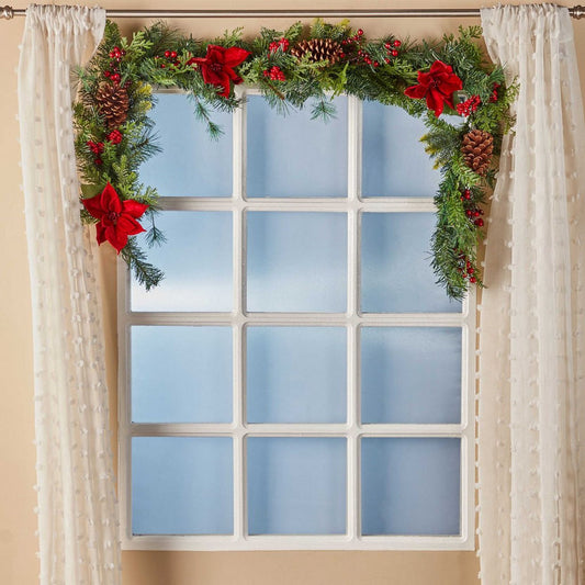 Decorative Christmas garland with red flowers and pine cones above a window.