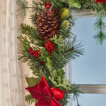 Christmas garland with pine cones, red berries, and a red flower in front of a window.