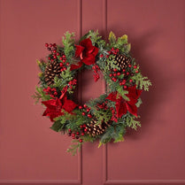Christmas wreath with red ribbons, berries, and pine cones on a red background
