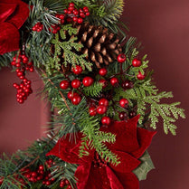 Christmas wreath with red berries, pine cones, and ribbons on a dark background
