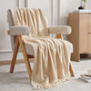 Beige blanket draped over a wooden armchair in a room with a light-colored wall and wooden cabinet.