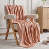 Pink blanket draped over a beige armchair in a room with a wooden cabinet and books.