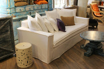 White sofa with decorative pillows in a room with wooden floor and furniture. New York Collection Sofa – Live in the Now | Vella Concept