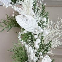 Decorative arrangement of greenery, white berries, and white stones on a neutral background