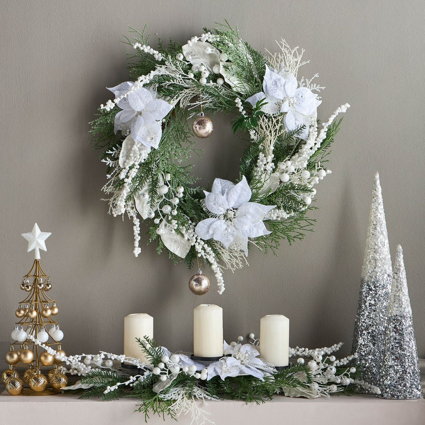 Decorative Christmas wreath with white flowers, candles, and festive trees on a neutral background