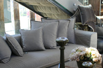 Gray sofa with decorative pillows and a small table with flowers in an outdoor setting. Cappadocia Collection Sofa – Simple, Serene & Timeless | Vella Concept