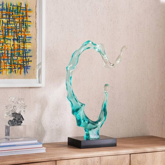 Abstract glass sculpture on a wooden surface with a painting in the background