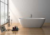 A white freestanding bathtub positioned on a wooden floor, with a window in the background and a black candle holder and bottles beside the tub.